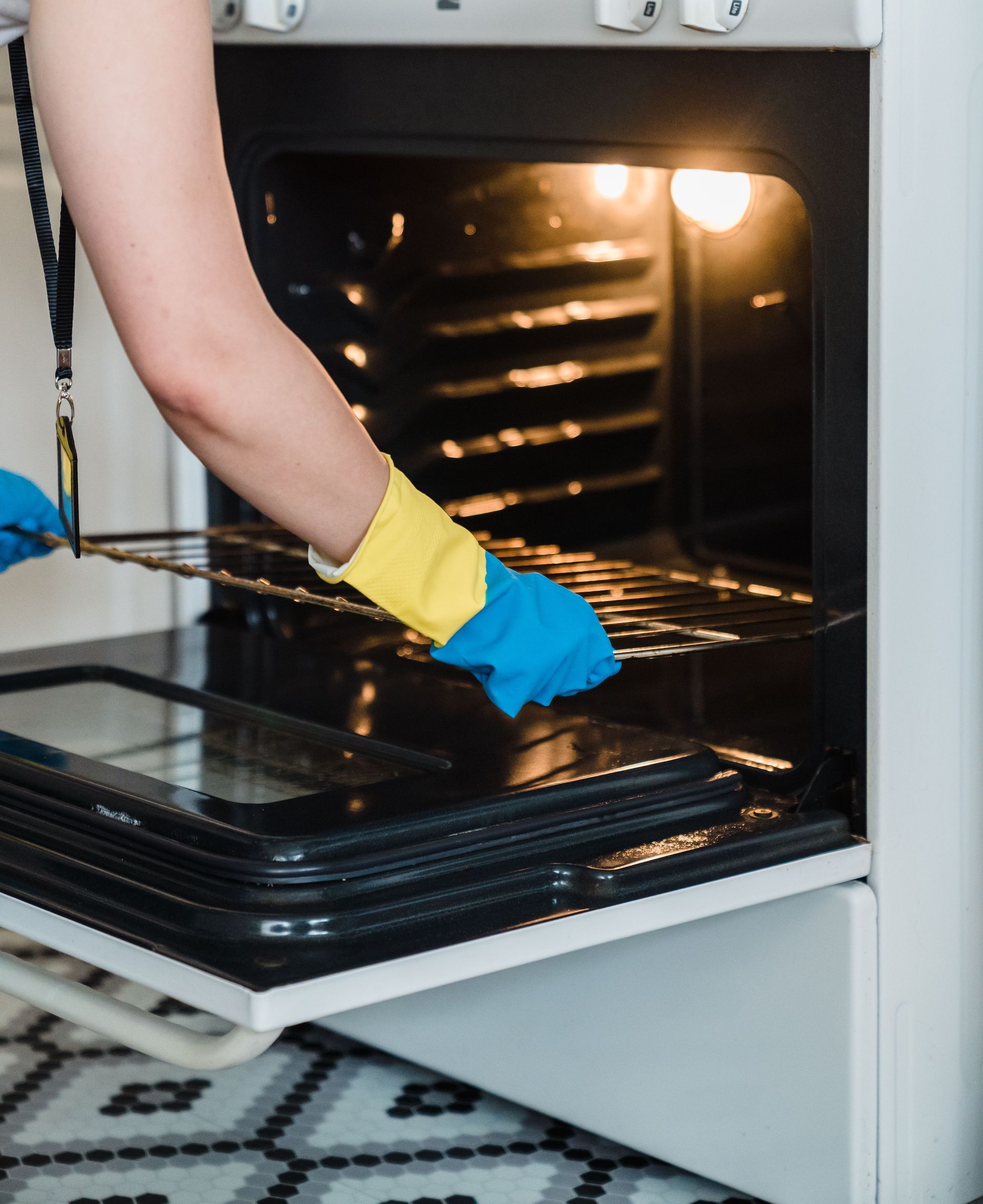 Adult woman cleaning an oven using protective rubber gloves indoors.