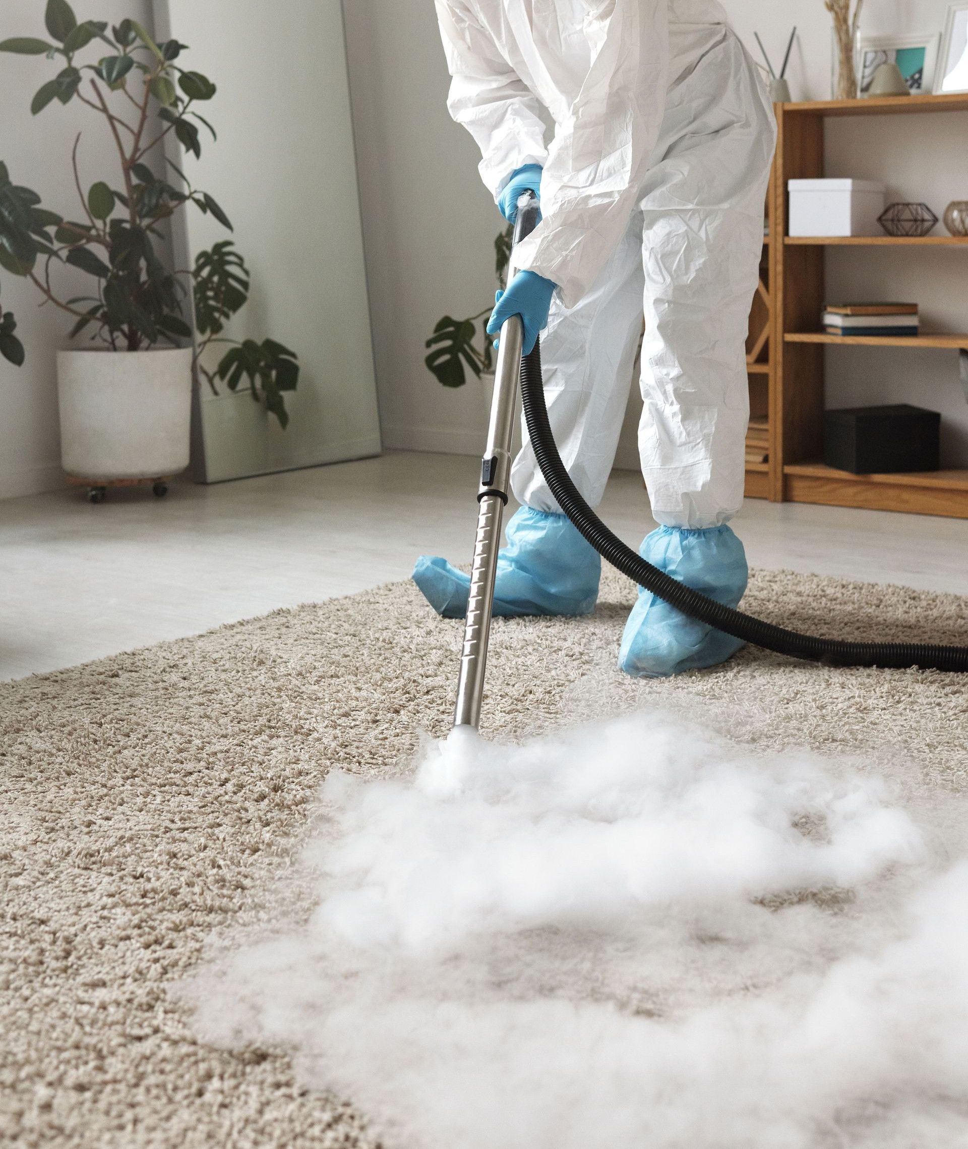 A person in protective gear disinfecting a carpet with a fumigation device indoors.